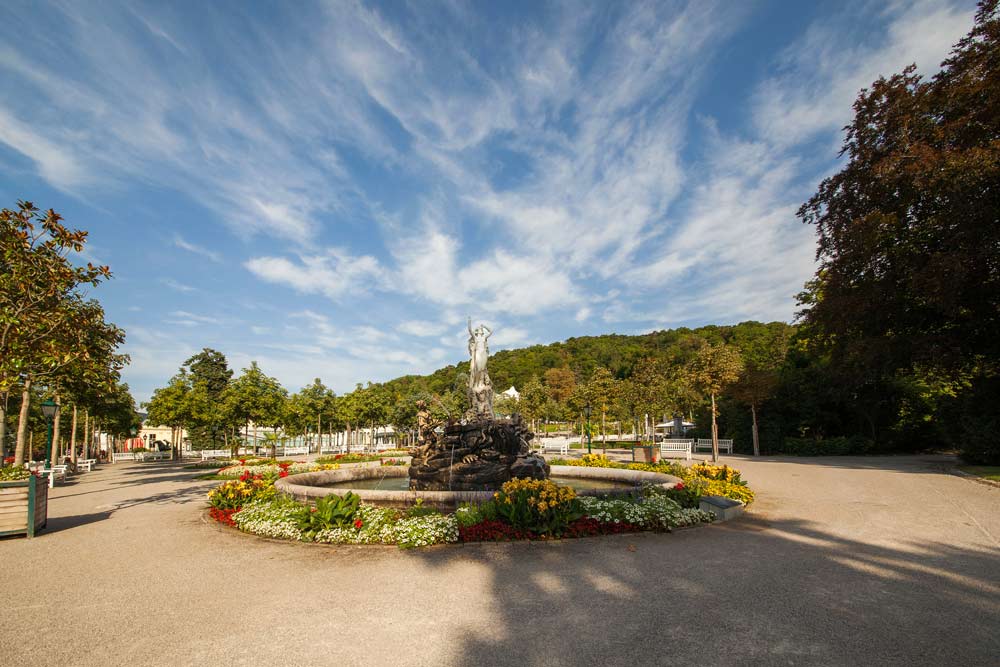 Brunnenanlage im Kurpark von Baden bei Wien mit Skulptur und umliegender Gartenanlage.